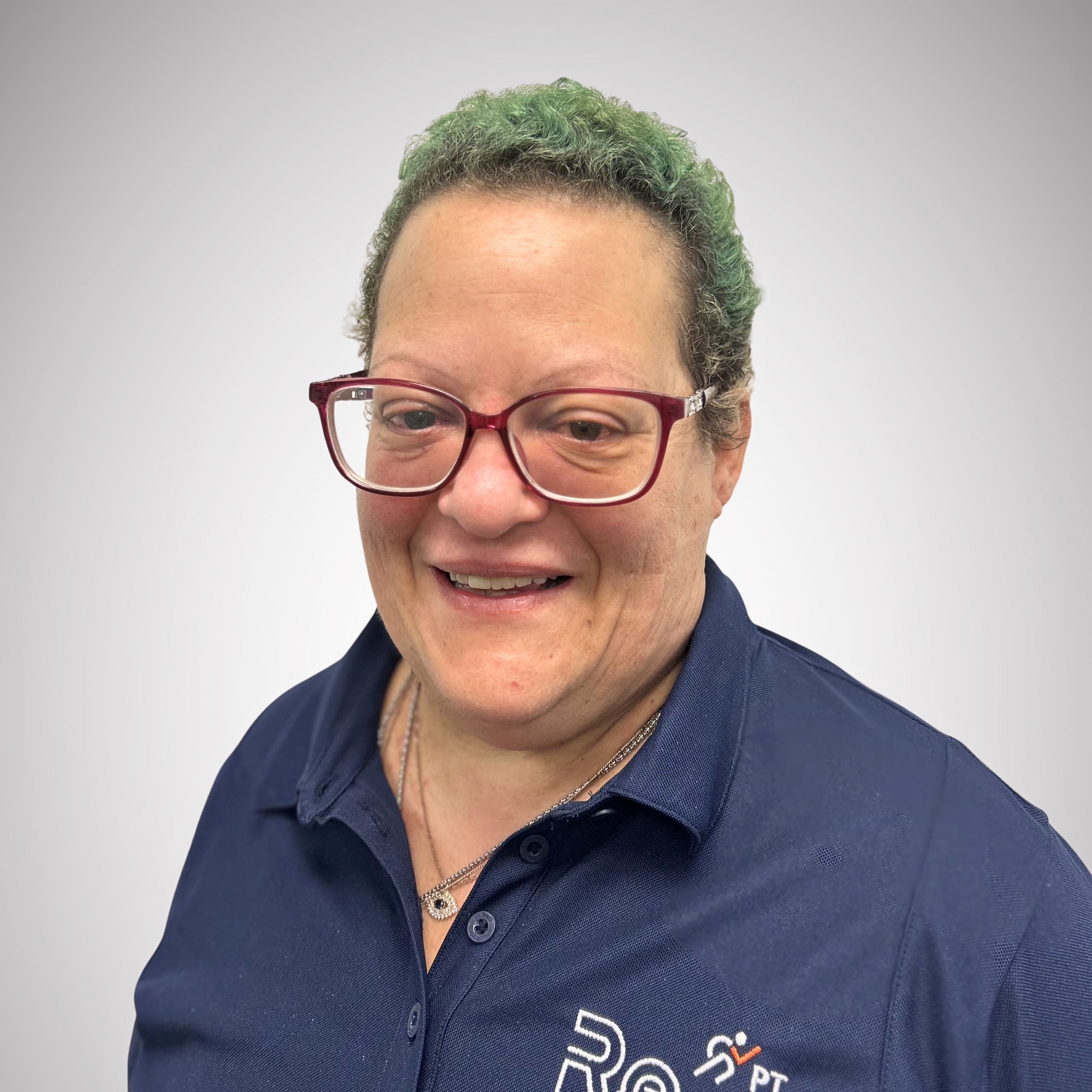 Smiling female physical therapist wearing a navy polo shirt with "ReEnvisionPT" logo, showcasing expertise in physical therapy services.